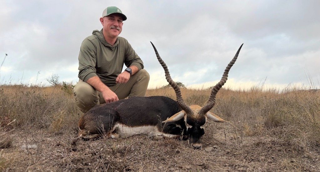 Hunter kneeling with trophy Blackbuck antelope on golden Texas grassland